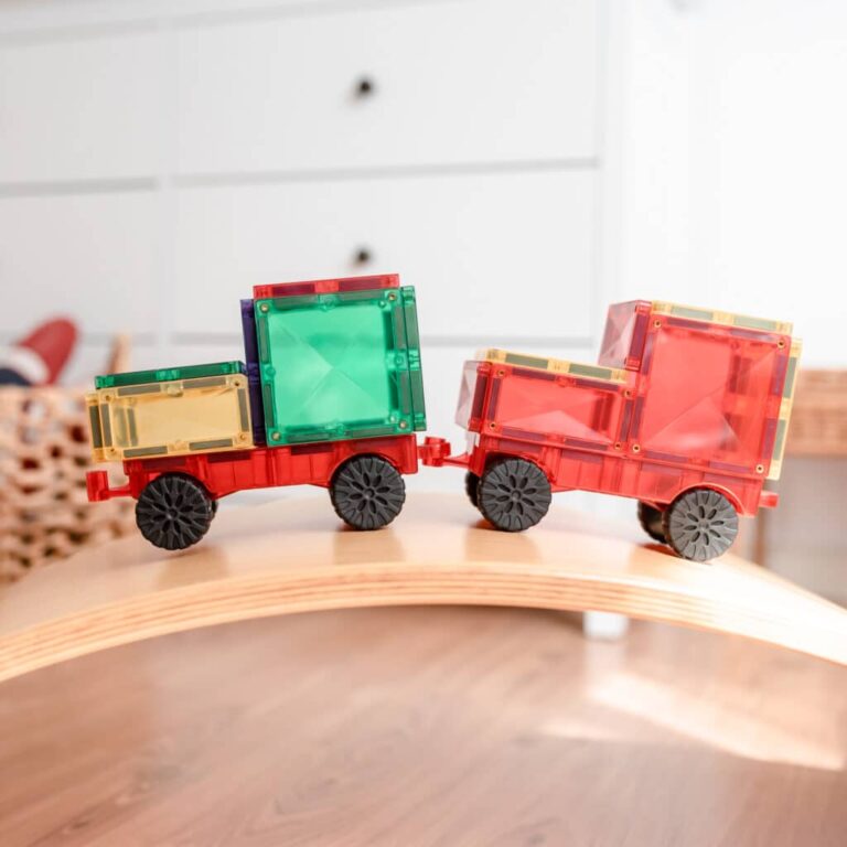 Două mașini din setul de construcție magnetic Connetix Rainbow pe o șină din lemn